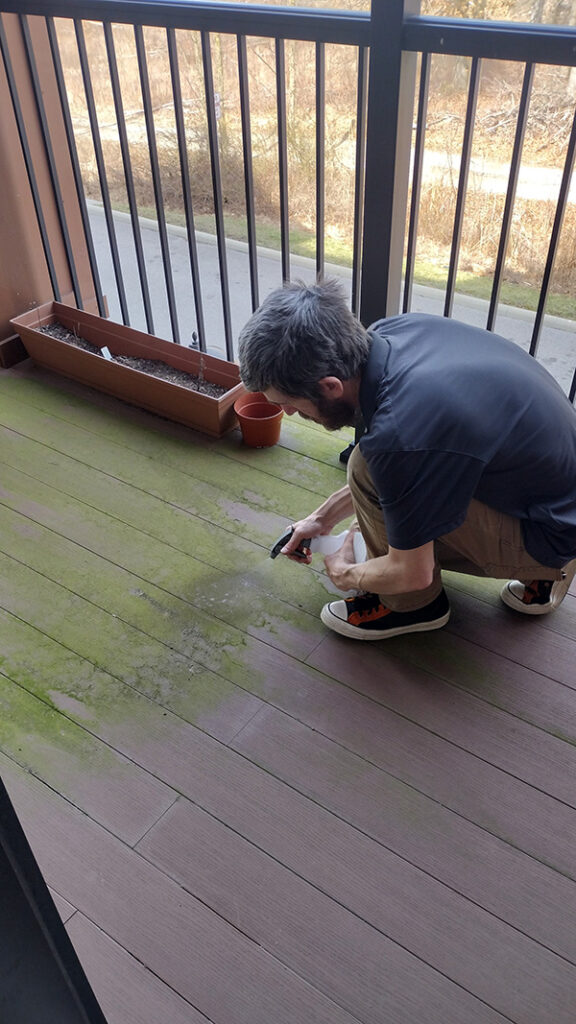 A man kneeling on a wooden deck, scrubbing away moss scum to keep the deck clean and tidy.