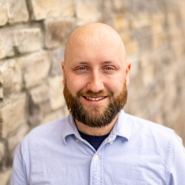 Keith Slabaugh, Operations Coordinator at Vitalia Stow, smiles in a light blue button-down shirt, standing in front of a textured stone wall in natural light.