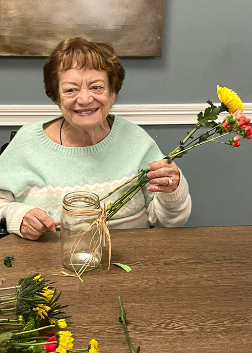 Senior resident arranging fresh yellow and red flowers in a mason jar during a spring floral activity.