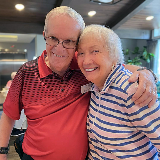 Smiling senior couple pose for a photo, the man's arm around the woman's shoulders.