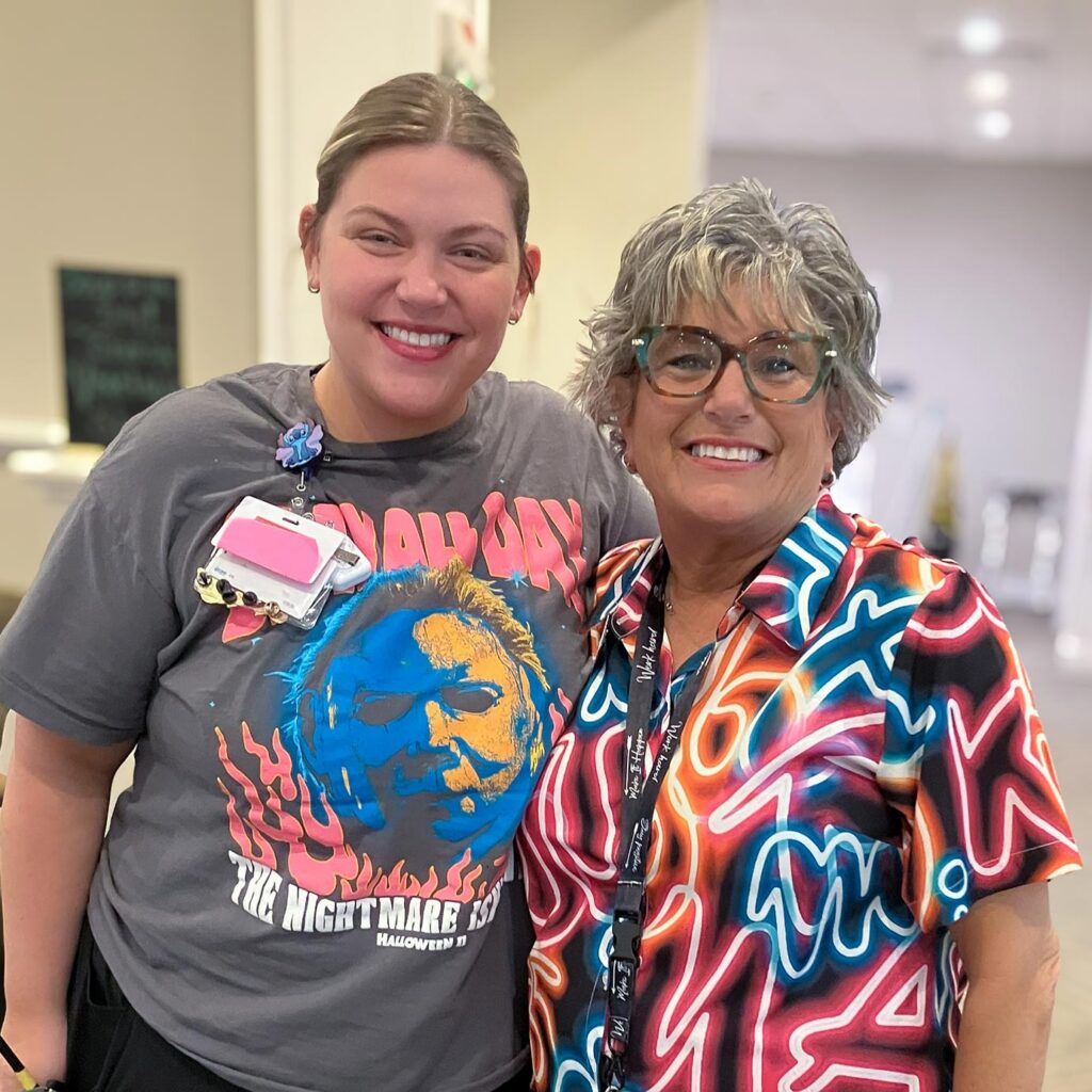 Two women, both in colorful clothing, smile for a photo.