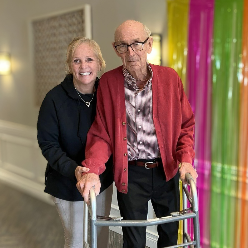 A senior man and loved one smile near a colorful party banner at Vitalia Stow.