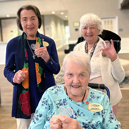 Three women on the resident ambassadors team at Vitalia Stow smile together while holding up heart figurines.